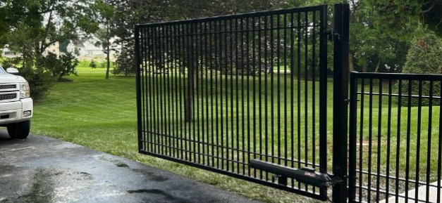 automatic-swing-driveway-gate-columbus-ohio Black vertical picket swing driveway gate with automatic opener installed on asphalt drive.